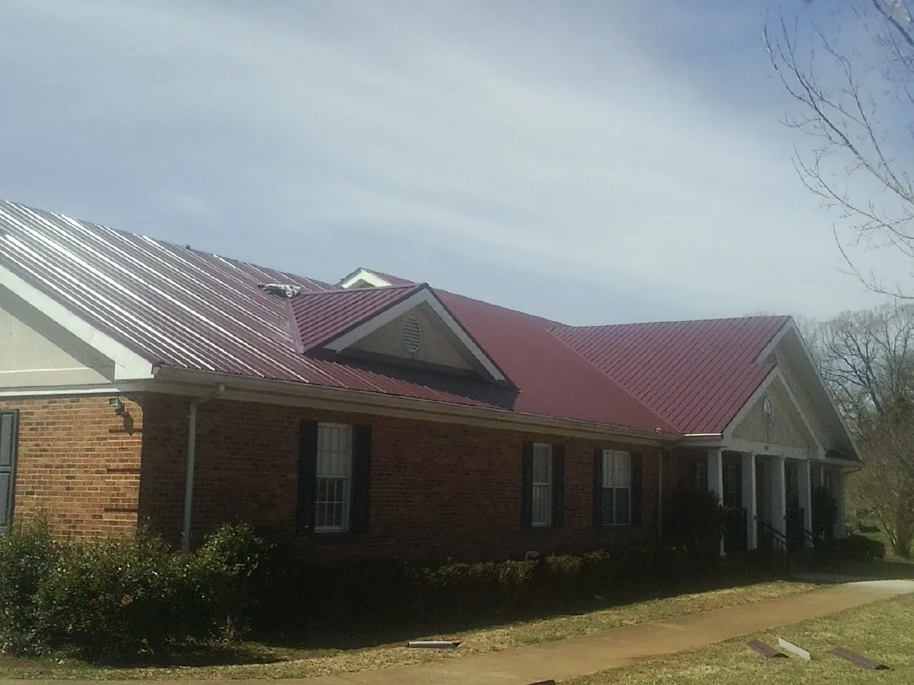 Red metal roof with gabled entries on a long brick building, from a Hail Damage Roof Repair job in Bethel