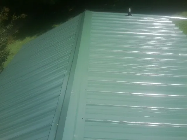 New green metal panels meeting at the ridge of a roof — Flat Roof Repair work by our crew in Bethel